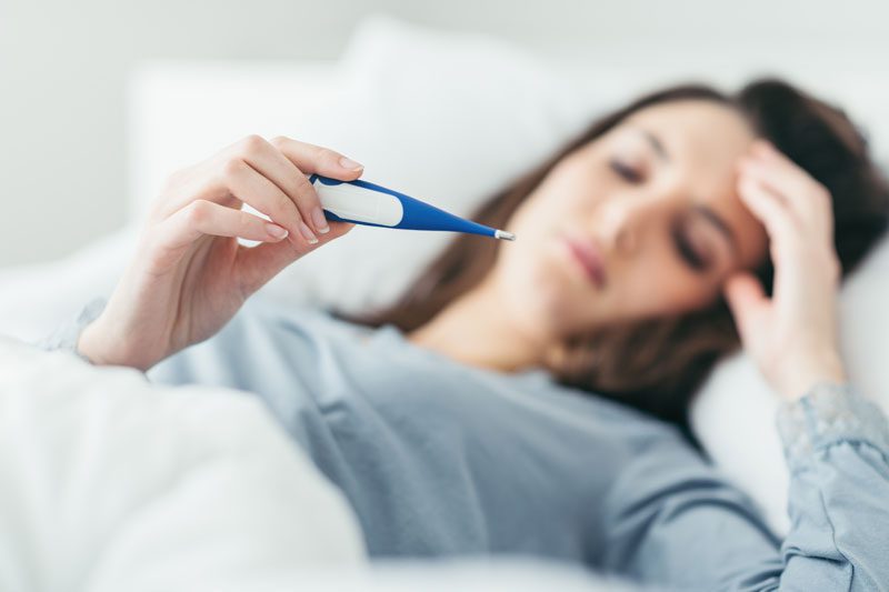 Riverview Hospice and Palliative Care LLC | Woman feeling sick lying in bed and taking her temperature with a thermometer