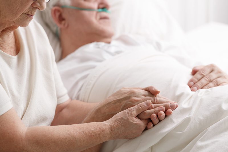 Riverview Hospice and Palliative Care LLC | woman holding her ill husband's hand as he lays in bed